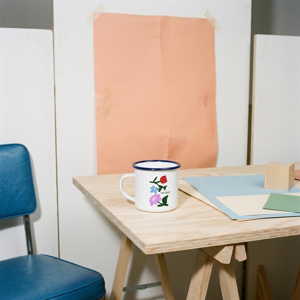 Mug émaillé Baby Flowers sur une table de bureau en bois avec chaise bleue – idée cadeau future maman