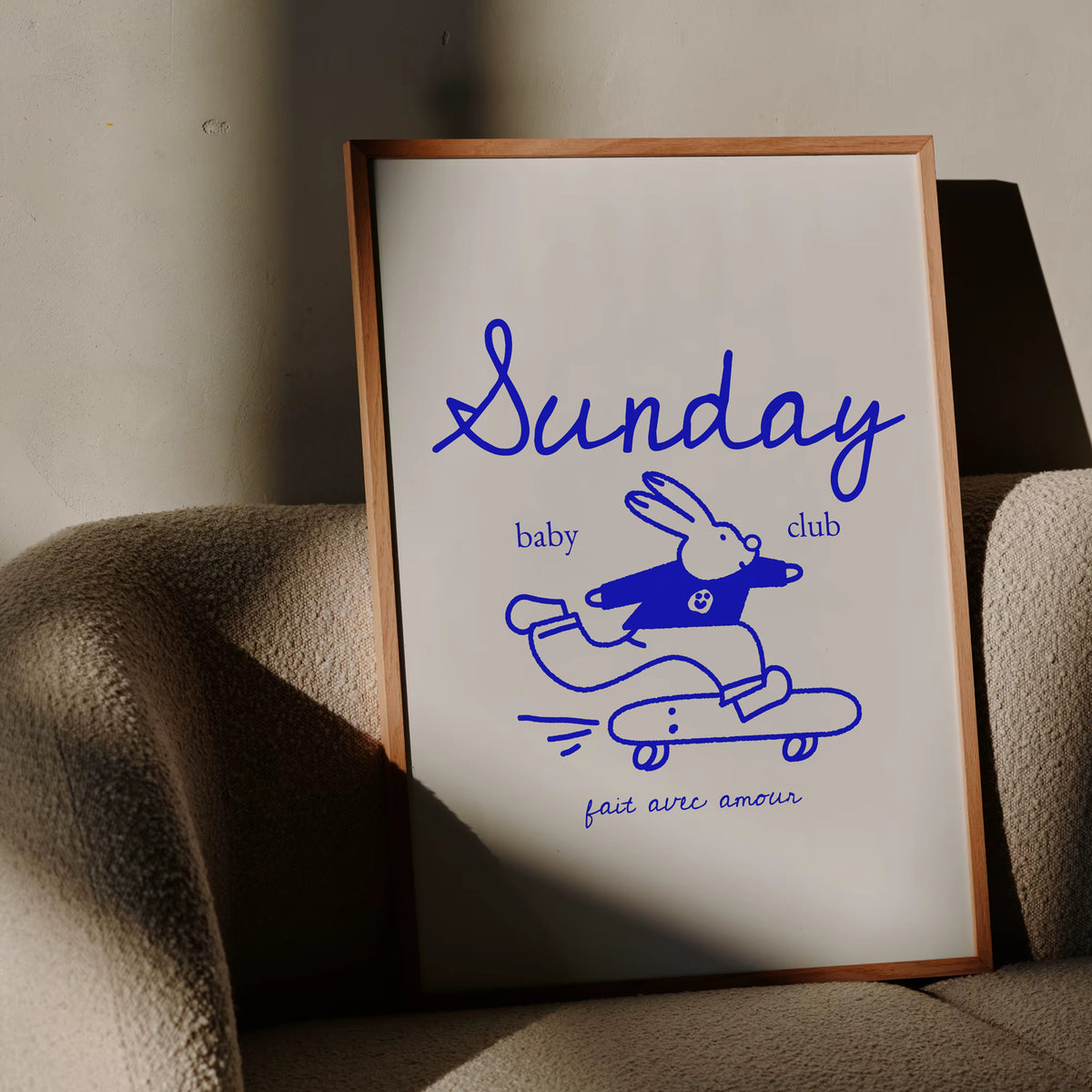 Affiche Sunday Baby Club au lapin sur skateboard bleu, encadrée et posée sur un fauteuil – déco chambre bébé