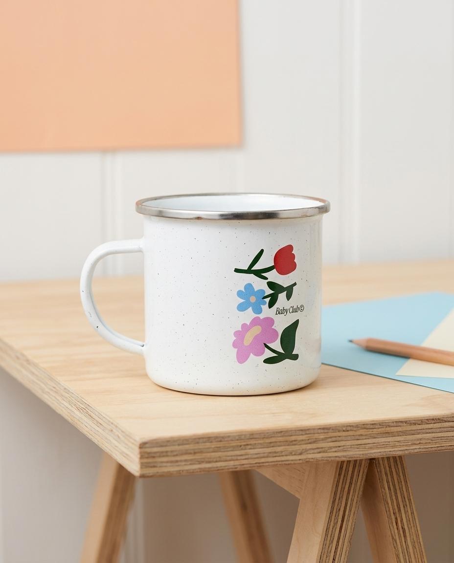 Mug émaillé blanc Baby Flowers illustré de fleurs rouge, bleue et violette, posé sur un bureau en bois – cadeau future maman