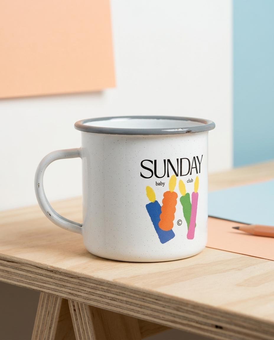 Mug émaillé blanc Sunday Baby Club illustré de bougies colorées, posé sur un bureau – cadeau grossesse